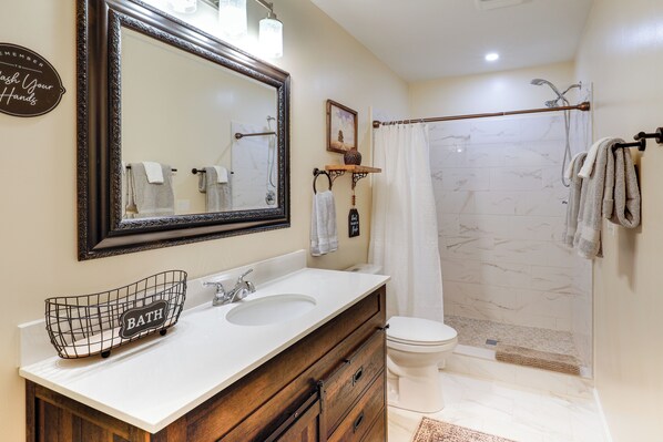 A bathroom with a large mirror, two sinks, a toilet, and a shower area. - Deck & Game Room! Lakefront Blue Ridge Mtn Gem (Deep Gap)