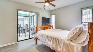 Un dormitorio con cama, ventilador de techo, televisor y puerta corrediza de vidrio que da a un patio.