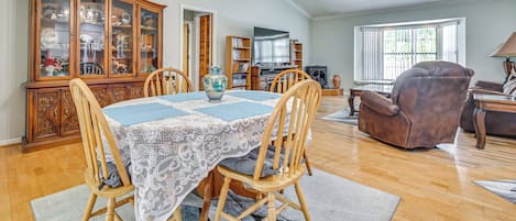 A spacious living room with a dining area, wooden furniture, a chandelier, and a ceiling fan.