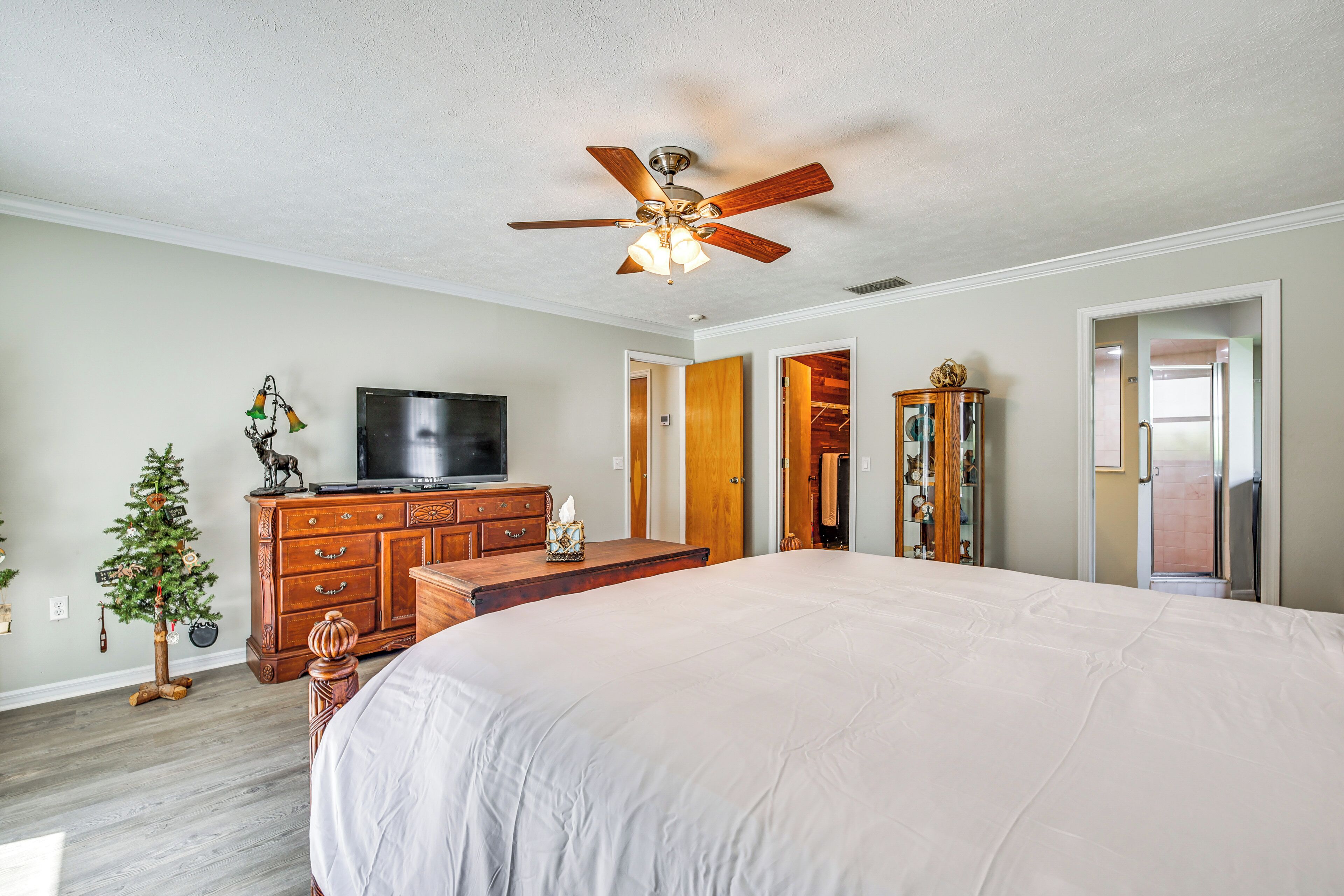 A bedroom with a large bed, wooden dresser, television, and a ceiling fan.