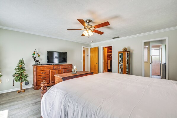 A bedroom with a large bed, wooden dresser, television, and a ceiling fan.