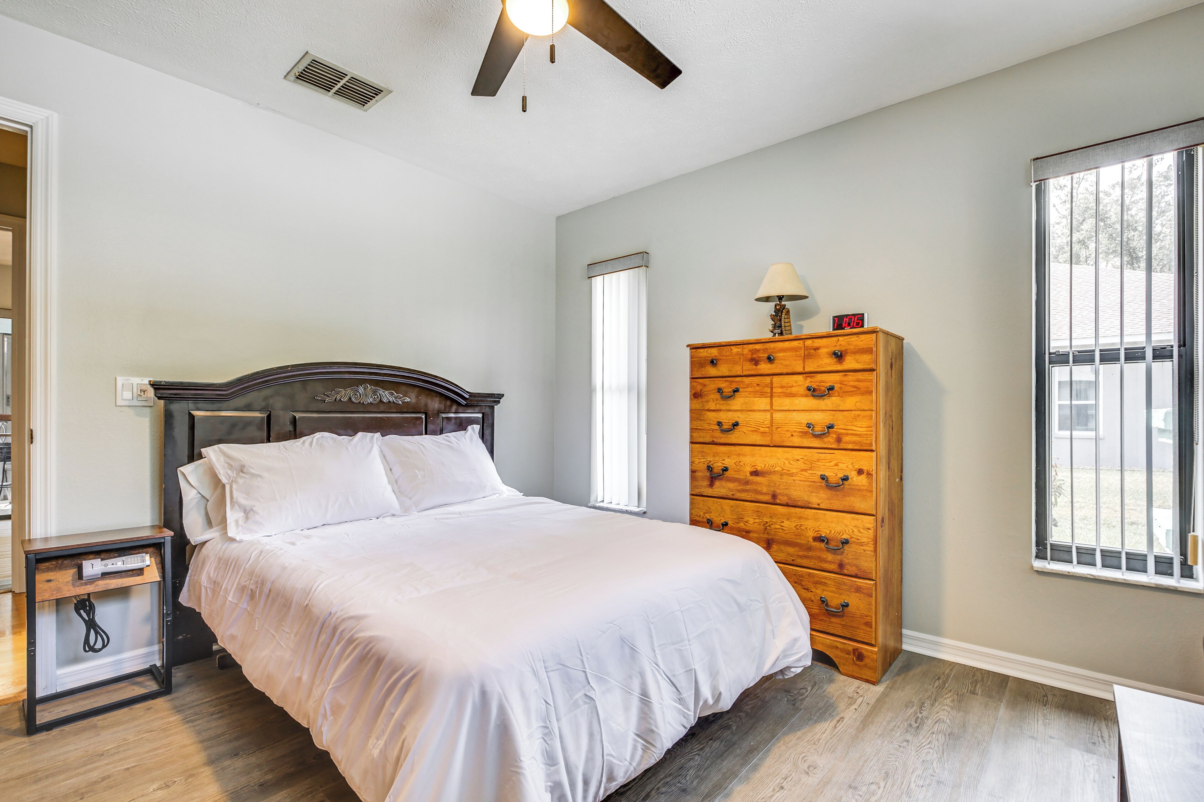 A bedroom with a bed, a wooden dresser, a nightstand, a window, and a ceiling fan.