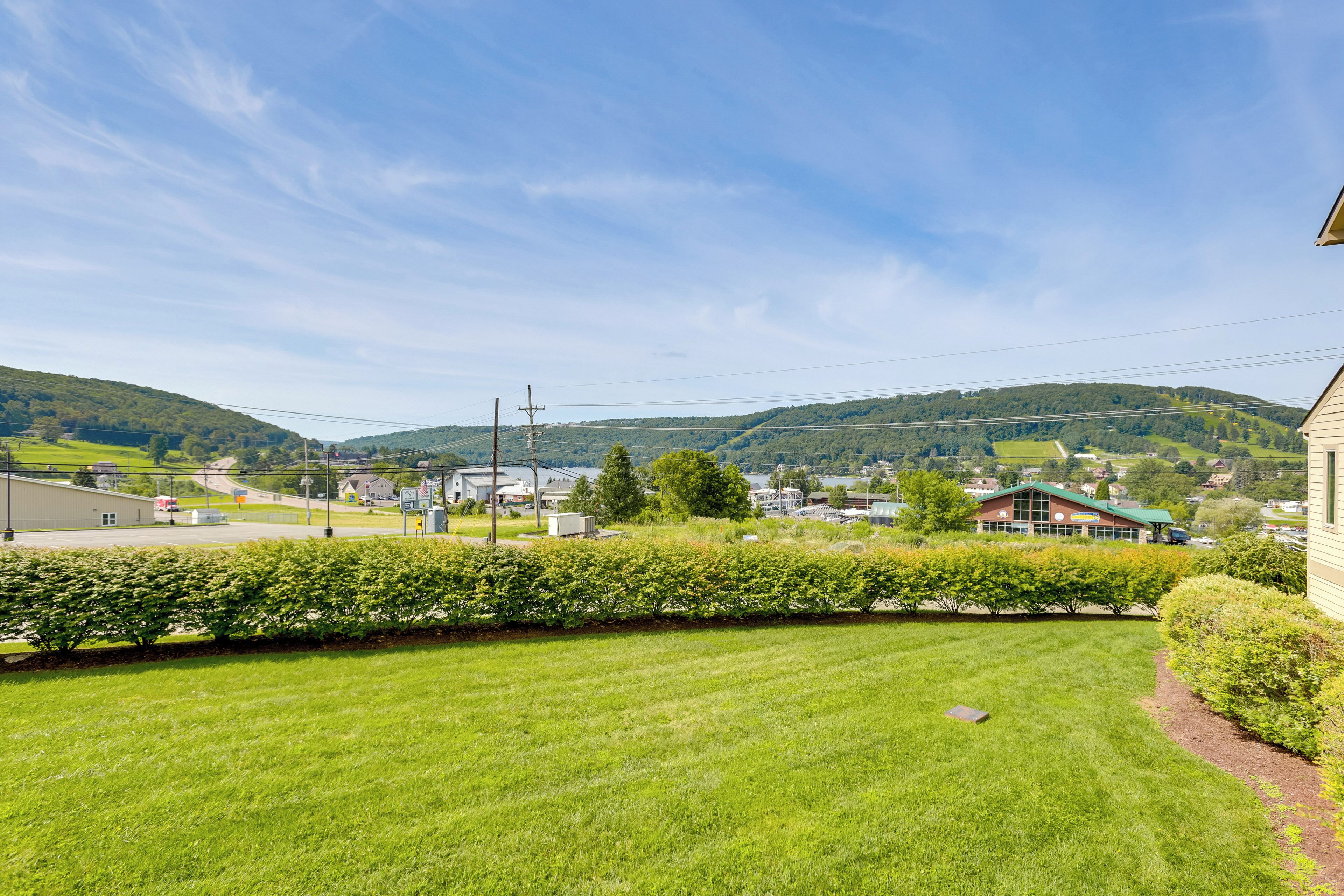 A residential area with a well-maintained lawn, a hedge, and a view of a town with buildings and hills in the background.