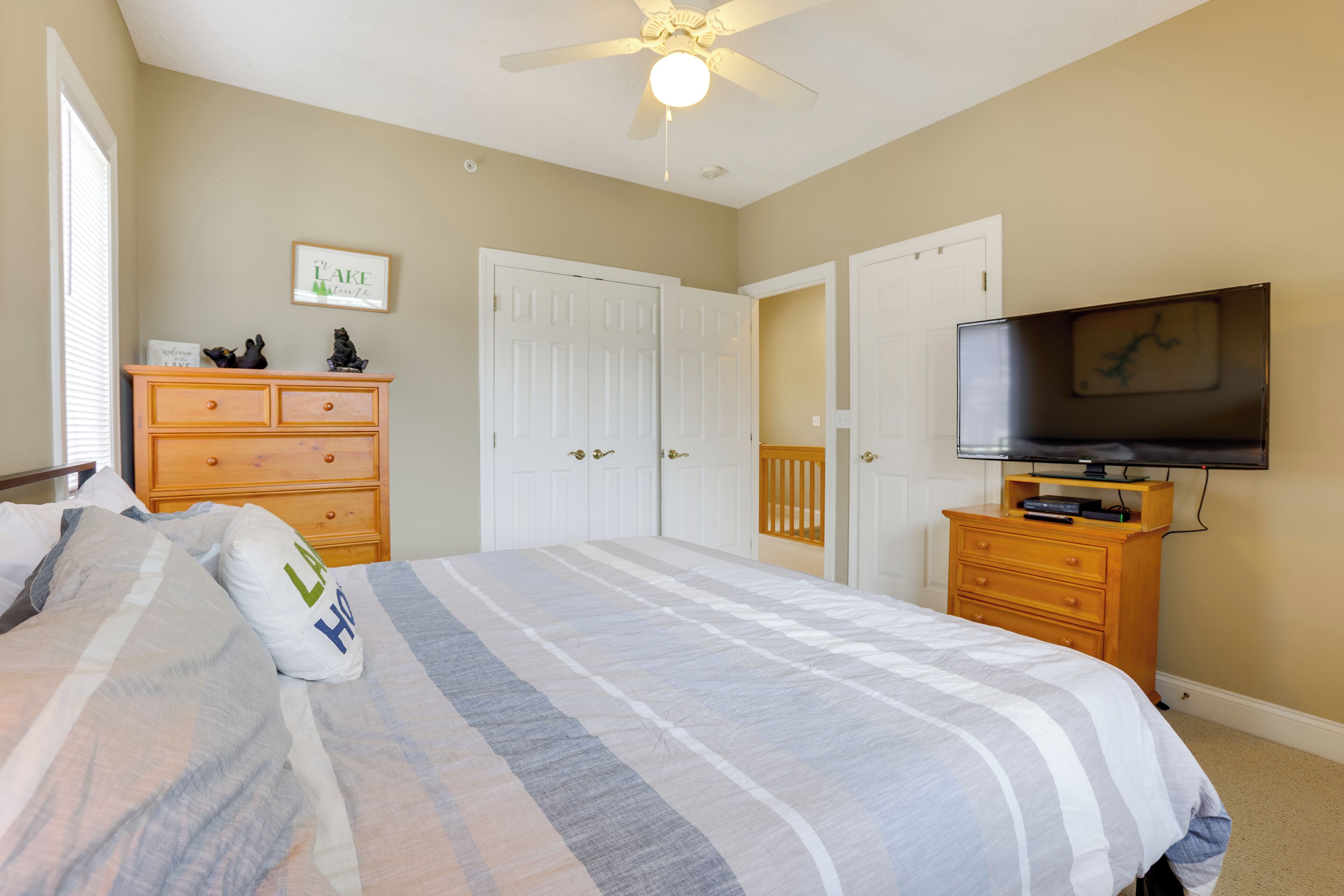 A bedroom with a bed, a dresser, a television, and a ceiling fan.