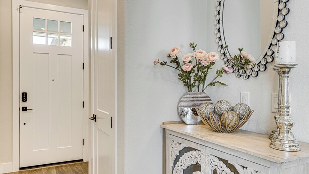 A hallway with a white door, a decorative mirror, a vase with flowers, and a silver candle holder. - Fenced-in Yard: Apt 7 Mi to Westfield Galleria (Roseville)