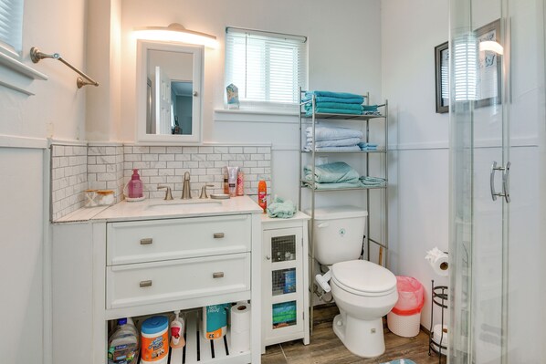 A modern bathroom with a white vanity, a toilet, a shower area, and a glass-enclosed toilet paper holder.