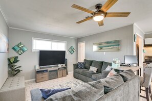 A living room with a flat-screen TV, a ceiling fan, a gray sofa, a coffee table, and a dining area with a table and chairs. - Private Bayfront Access 10 Mi to Galveston Beaches (Hitchcock)