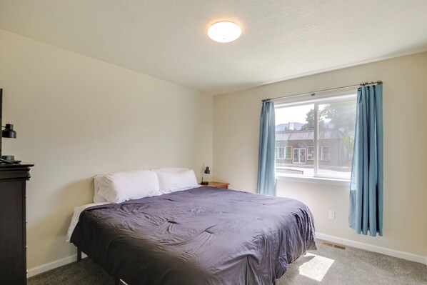Une chambre à coucher comprenant un lit, une table de chevet, une commode, une fenêtre avec des rideaux et un luminaire au plafond.