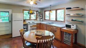 A kitchen with wooden cabinets, a dining table with chairs, a refrigerator, stove, microwave, and hanging pots. - Lakeside Getaway w/ Dock: West Battle Lake Cabin (Clitherall)