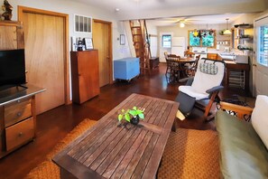 A living room with a wooden coffee table, a sofa, a TV, a kitchen area with a stove, and a dining table with chairs. - Lakeside Getaway w/ Dock: West Battle Lake Cabin (Clitherall)