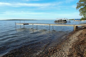 A calm lake with a dock extending into the water, surrounded by pebbles and vegetation. - Lakeside Getaway w/ Dock: West Battle Lake Cabin (Clitherall)