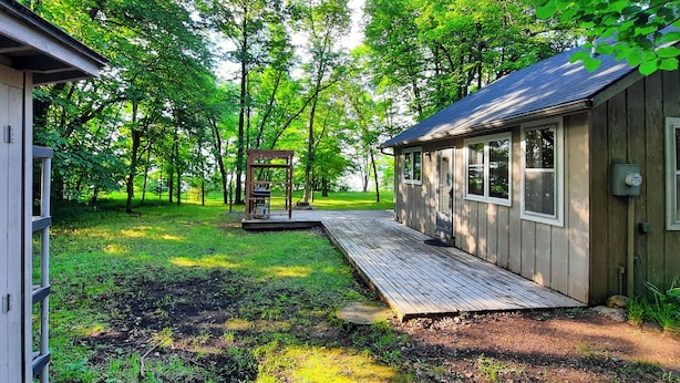 A wooden cabin with a deck, surrounded by trees. - Lakeside Getaway w/ Dock: West Battle Lake Cabin (Clitherall)
