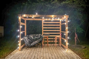 A wooden pergola structure with string lights, a covered grill, and a table with a chair. - Lakeside Getaway w/ Dock: West Battle Lake Cabin (Clitherall)