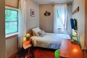 A bedroom with a bed, a bedside table with a lamp, a small stool, a wooden nightstand, a wall-mounted coat rack, and a window with curtains. - Lakeside Getaway w/ Dock: West Battle Lake Cabin (Clitherall)