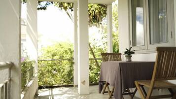 Un balcon avec une table et des chaises, une plante en pot et une vue sur la verdure.
