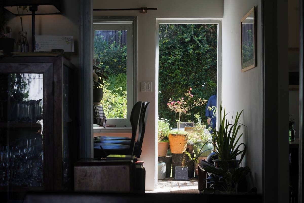A room with a view of a garden through a doorway, a chair, a table, and a potted plant.