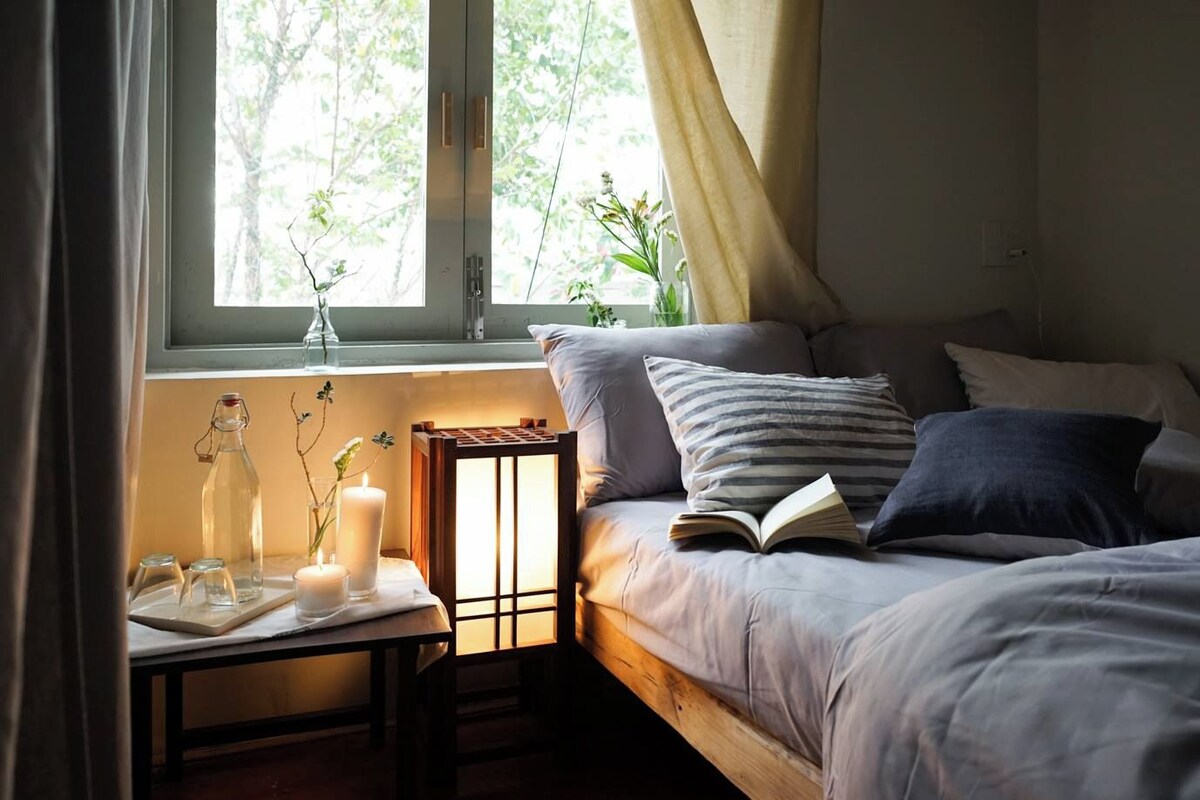 A cozy bedroom with a bed, bedside table, and a window with curtains.