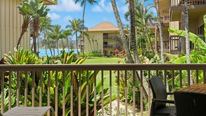 A hotel with a balcony, tropical plants, and a view of the ocean.