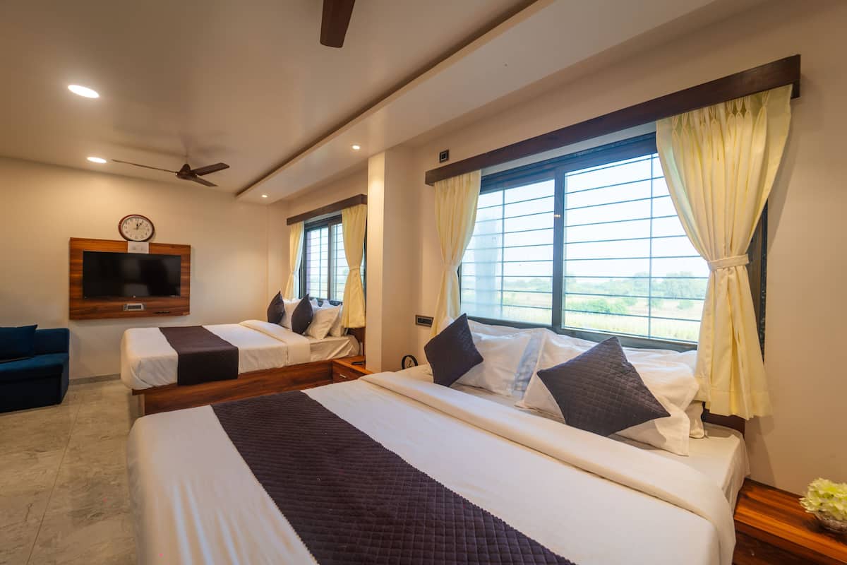 Quarto de hotel com duas camas, televisão de tela plana na parede, ventilador de teto e grandes janelas com cortinas.