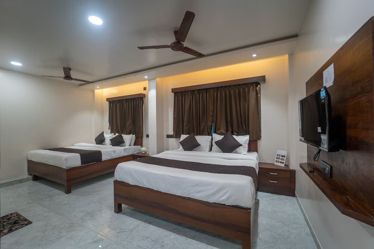 Quarto de hotel com duas camas, um ventilador de teto, uma televisão e uma cômoda de madeira.