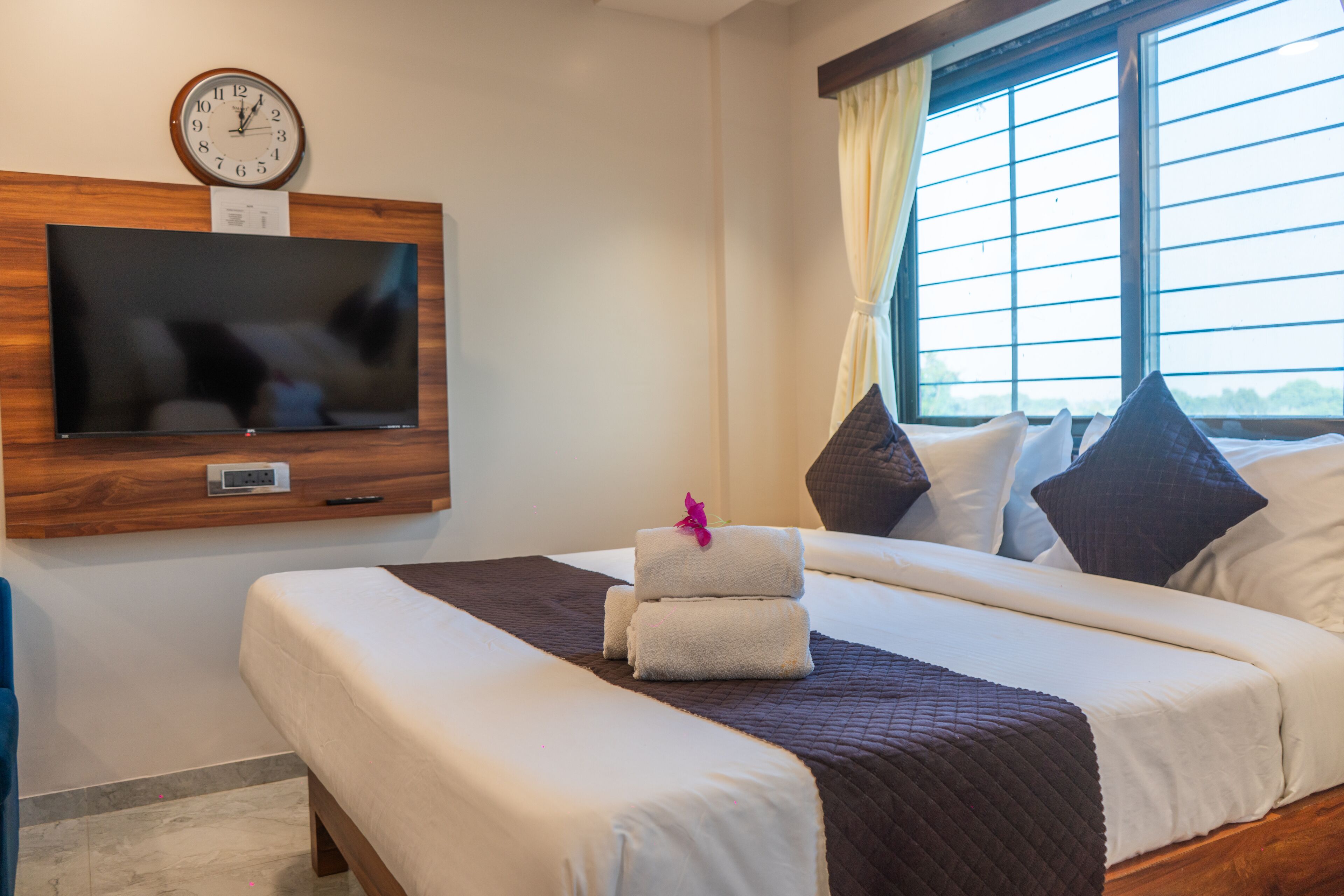 A hotel room with a bed, a TV mounted on the wall, and a window with curtains.