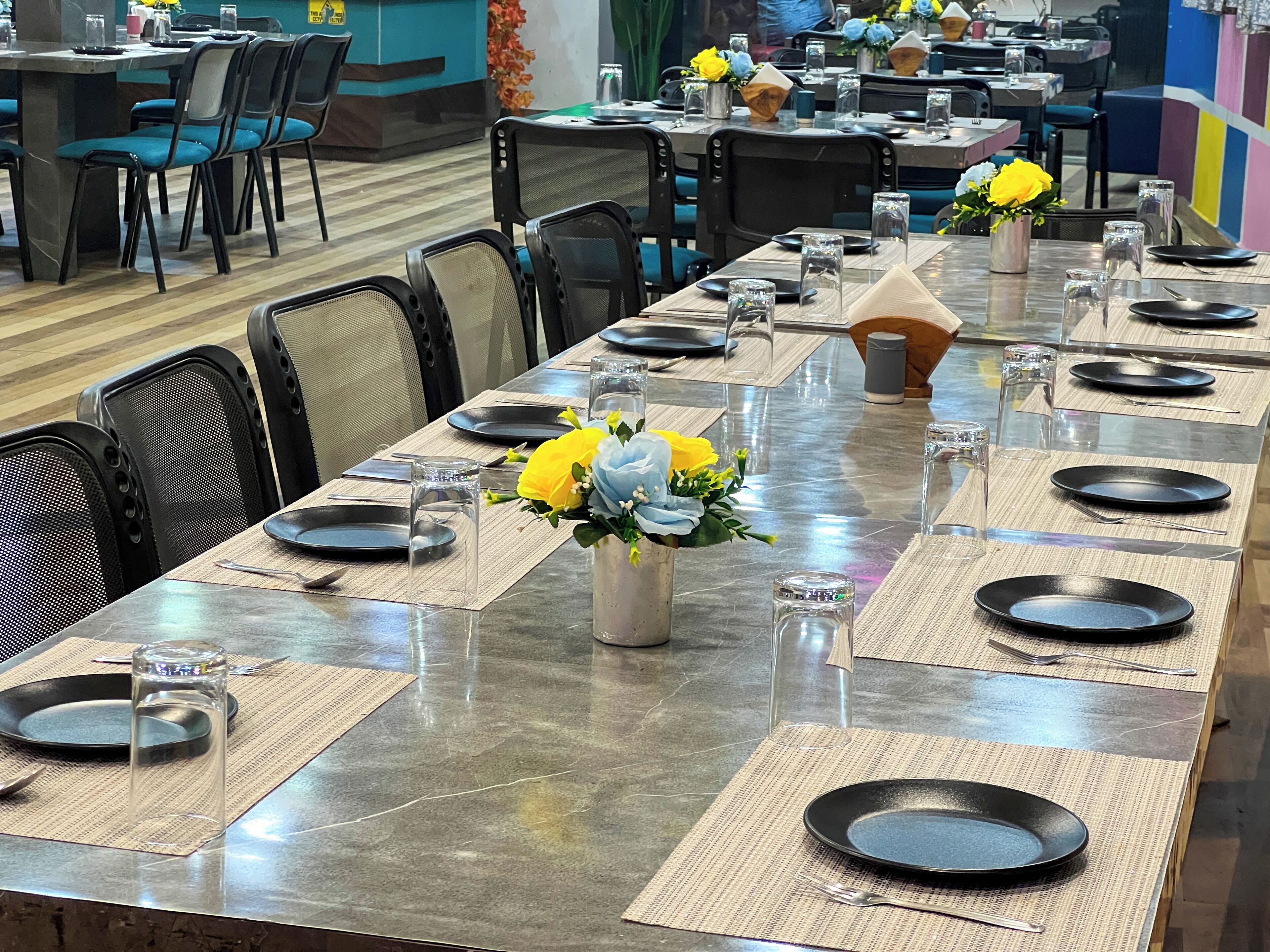 A restaurant with long tables set for dining, featuring clear glassware, black plates, and floral centerpieces.