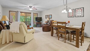 Una sala de estar con un sofá, una mesa de comedor con sillas, un ventilador de techo y un televisor.