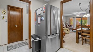 Una cocina con un refrigerador de acero inoxidable, un cubo de basura y una puerta de madera.