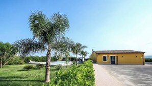 A yellow building with a tiled roof, a paved driveway, and a swimming pool in the background. - House Lumia White Zagara (Sicilia)