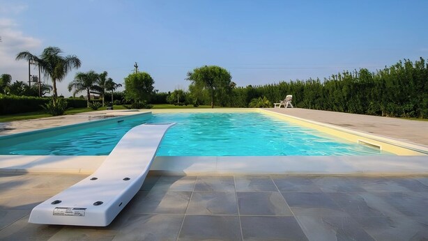 A swimming pool with a sun deck, surrounded by greenery and a clear sky. - House Lumia White Zagara (Sicilia)