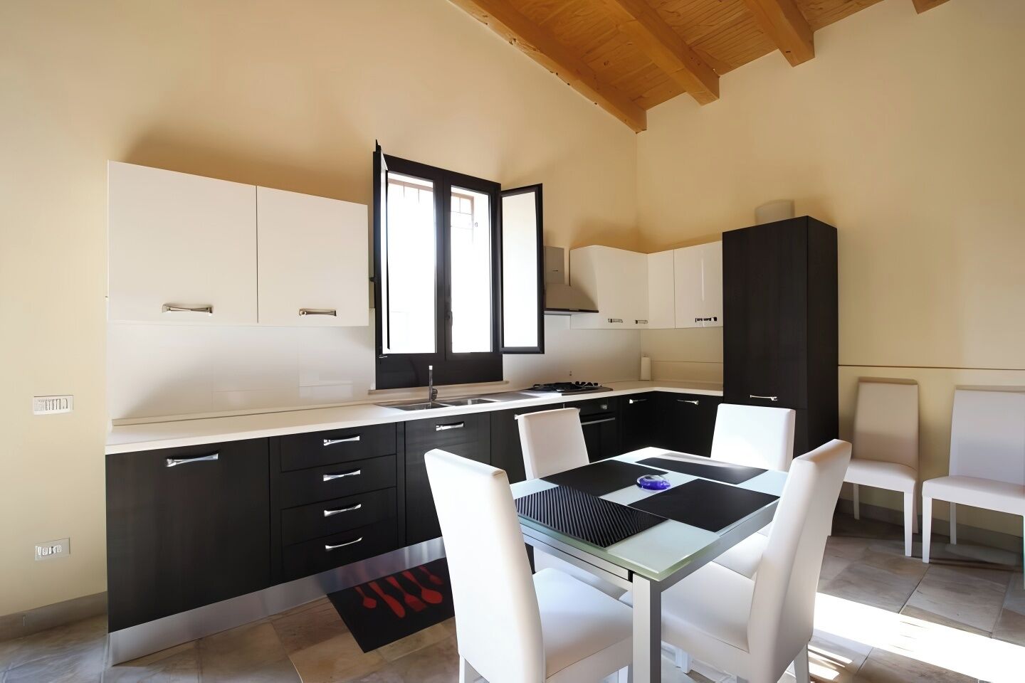 Une cuisine moderne avec des meubles de rangement noirs et blancs, une table à manger avec des chaises blanches et une grande fenêtre qui laisse entrer la lumière naturelle.