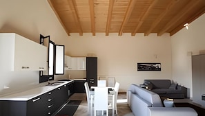 Una cocina moderna con armarios negros, encimera blanca y un comedor con sofá gris y sillas blancas.