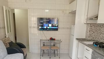 A compact kitchen with a washing machine, a dining table with chairs, and a flat-screen TV mounted on the wall.