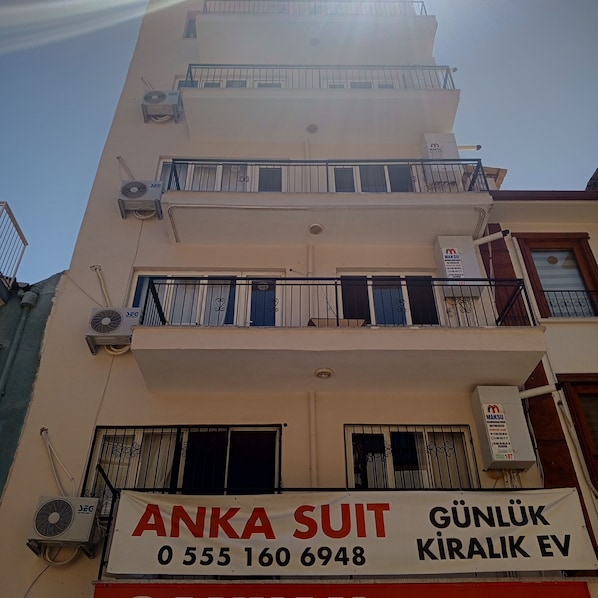 A multi-story building with balconies, air conditioning units, and a signboard for 'ANKA SUIT' with contact information.