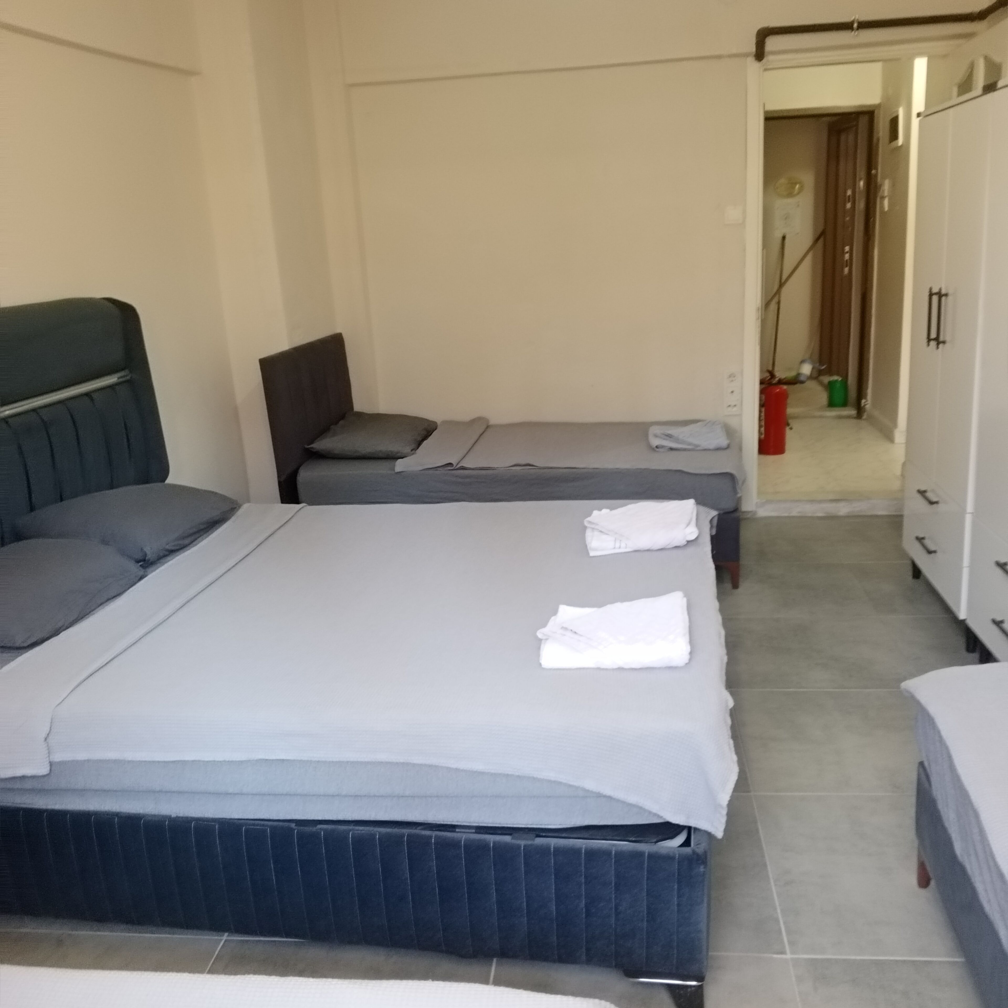 A hotel room with two beds, a wardrobe, and a bathroom visible in the background.