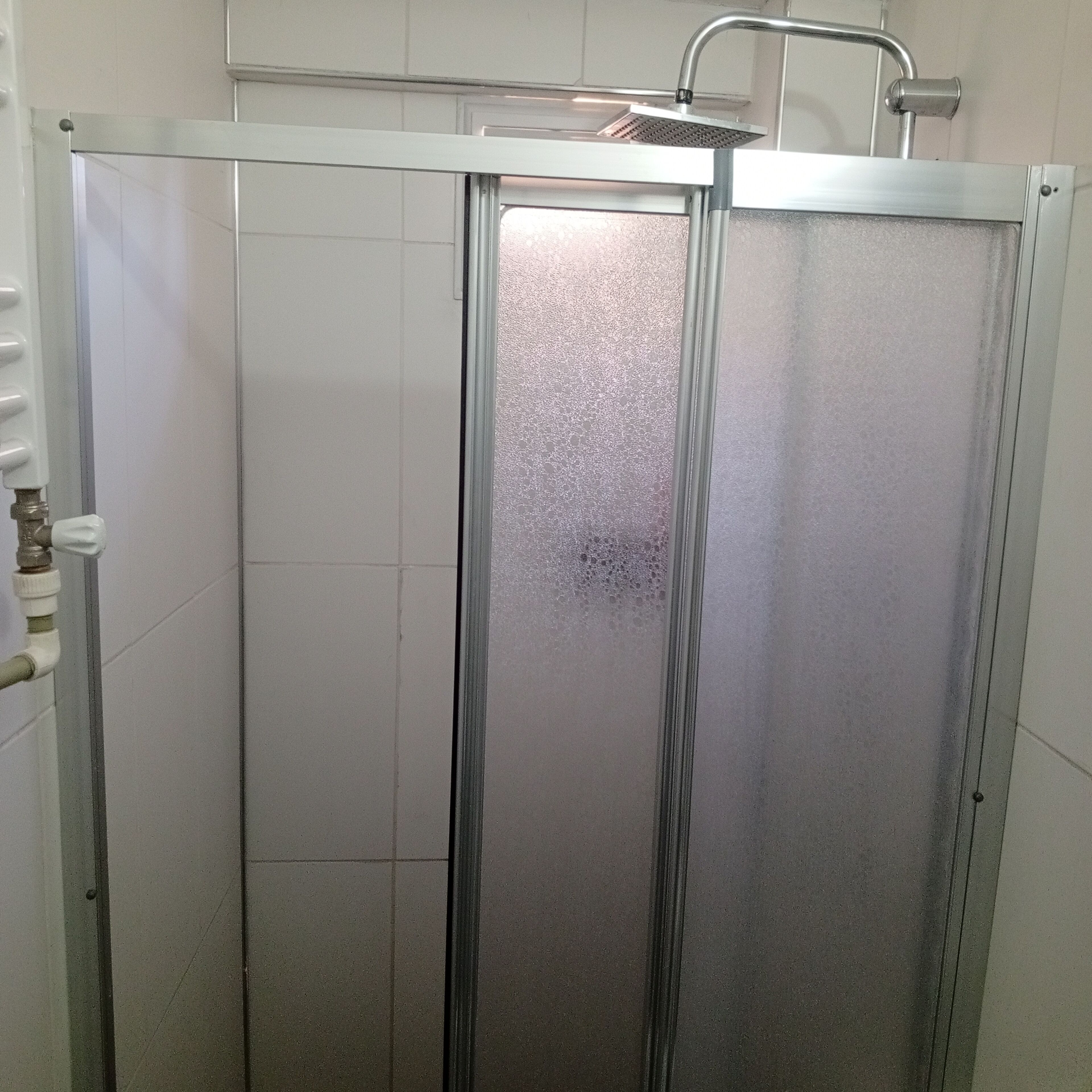A shower enclosure with a frosted glass door, a metal handle, and a faucet.