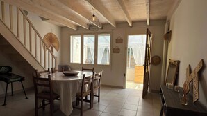 Un comedor con una mesa redonda, sillas, una escalera y vistas a través de las ventanas.