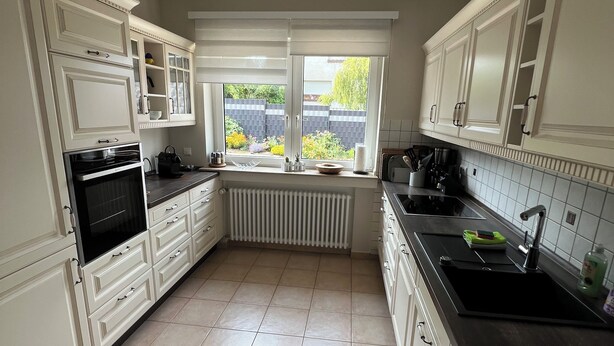Una cocina con armarios blancos, encimera negra y ventana con vistas a un jardín.