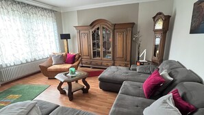 Una sala de estar con un sofá seccional gris, un mueble de madera, una lámpara de pie y un reloj grande en la pared.