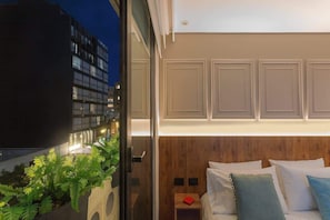 A modern hotel room with a large bed, a wooden headboard, and a view of the cityscape at night.