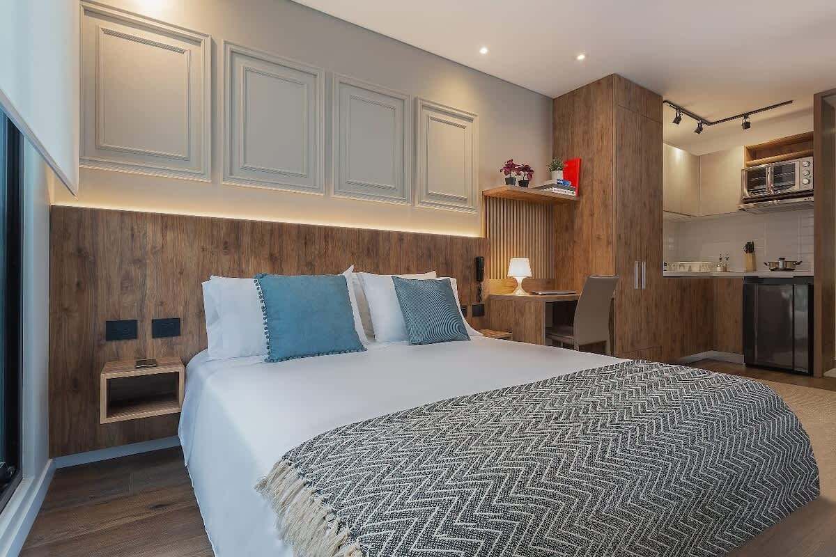 Une chambre d’hôtel moderne dotée d’un grand lit, d’une tête de lit en bois et d’un coin cuisine intégré.