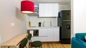 A compact kitchen with white cabinets, a stainless steel refrigerator, a red pendant light, a wooden table, and a teal sofa. - NOK Perfect 1 BR in Centro Historico (Bogotá)