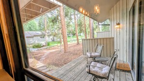 A wooden deck with two metal chairs and a bench, overlooking a backyard with trees and a lawn. - Peaceful Retreat.  Outdoor Pool / Indoor Hot Tub (Keystone)