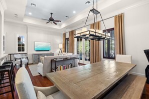 A spacious living room with a large wooden dining table, a sofa, and a television on the wall.