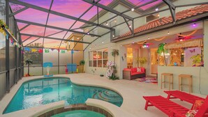 Una piscina interior con techo de cristal, sillones reclinables rojos y un interior colorido.