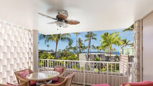 A balcony with wicker furniture, a ceiling fan, and a view of palm trees and buildings.