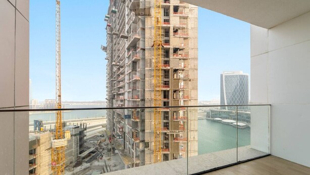 Un immeuble de grande hauteur en construction, avec vue sur un port et un pont en arrière-plan.