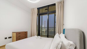A modern hotel room with a large bed, a wooden dresser, and a view of a cityscape through a large window. - FIRST CLASS | 1BR |  Waterfront Bliss (Al Maryah Island)
