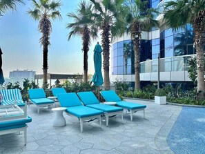 A rooftop pool area with blue lounge chairs and a palm tree.