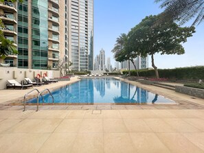 A swimming pool with lounge chairs and a lifebuoy, surrounded by high-rise buildings and greenery.